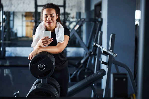 Leende vacker kvinna med mobiltelefon i gymmet — Stockfoto