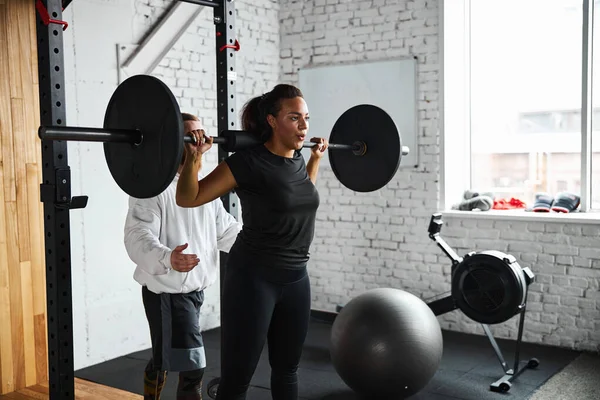 Mujer joven haciendo ejercicio con barra de pesas en el gimnasio — Foto de Stock