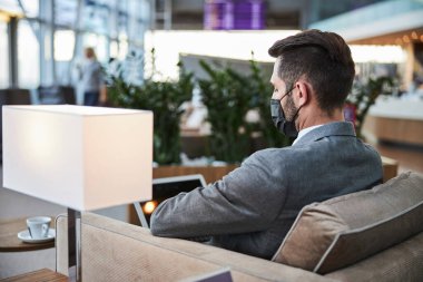 Koyu renk saçlı takım elbiseli adam koridorda tek başına oturuyor.