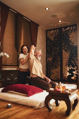 Neşeli Asyalı kadın geleneksel jimnastik için erkeğe yardım ediyor.