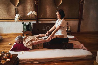 Asyalı terapist masaj stüdyosunda kır saçlı adamı tedavi ediyor.