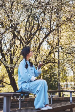 Kung fu üniformalı kadın çay içerken doğanın tadını çıkarıyor.