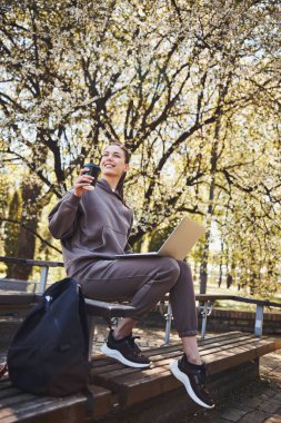 İyimser kadın dışarıda laptop kullanırken kahve içiyor.