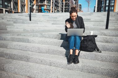 Dizüstü bilgisayarlı gülümseyen kadın beton merdivenlerde oturuyor.