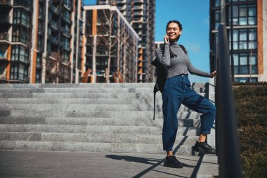 Telefon konuşması sırasında metal korkuluklara yaslanan neşeli kadın.