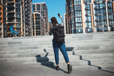 Saçları örgülü Afrikalı Amerikalı turist kendini gökdelenlere karşı fotoğraflıyor.