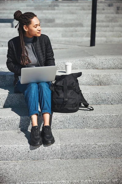 Beautiful pensive woman with cornrows seated on the concrete stairs — 图库照片