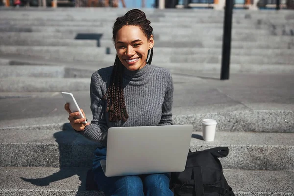 Smiling woman with gadgets sitting on the concrete steps outdoors — 스톡 사진