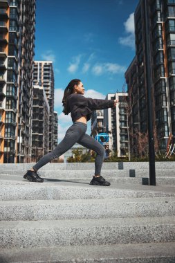 Gülen sporcu kadın beton merdivenlerde ısınıyor.