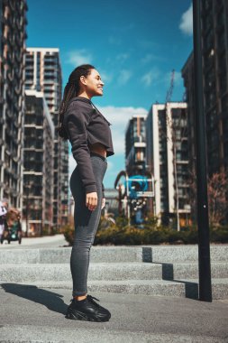Saçları örgülü neşeli sporcu kadın uzaklara bakıyor.