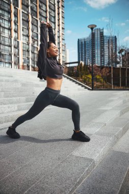 Gülümseyen atletik kadın dışarıda esneme egzersizi yapıyor.
