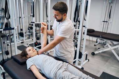 İyileşme kliniğindeki fizyoterapistten omuz manuel terapisi gören bir kız. Spor sakatlığı rehabilitasyonu