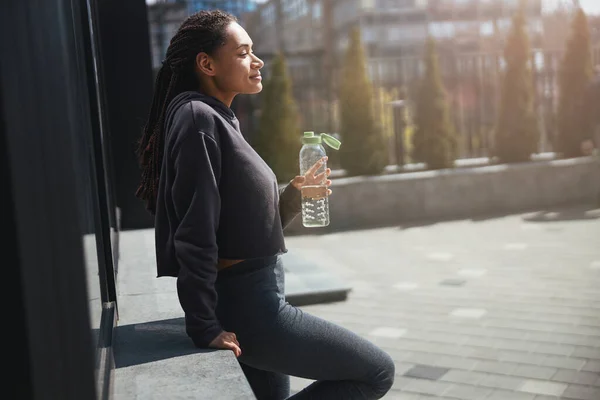 Zamyšlená žena s plastovou lahví vody zírající před sebe — Stock fotografie