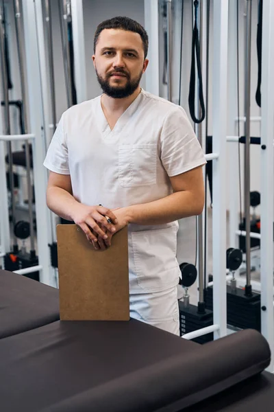 Portrait of professional masseur with clipboard of history of his patient. Confident young doctor — Stock Fotó