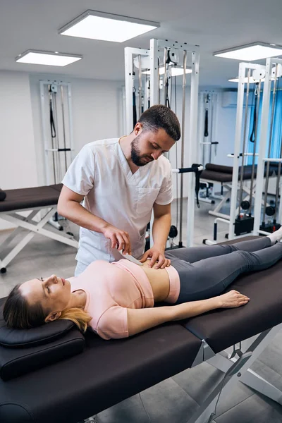 Specialist physiotherapist massaging woman with IASTM instrument in rehabilitation center — стокове фото