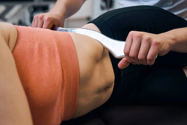 Close-up of woman lying on side on physiotherapy treatment. Chiropractor presses abs with IASTM tool — 스톡 사진