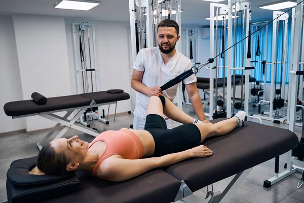 Jonge vrouw trainen beenspieren en gewrichten onder toezicht van artsen op massagetafel — Stockfoto