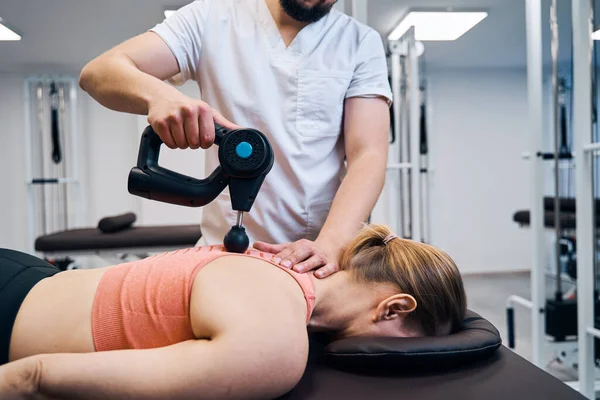 Fysiotherapeut behandelt vrouw wervelkolom en rug met masserende percussie-apparaat. Fysiotherapie — Stockfoto