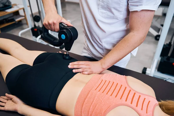 Fysiotherapeut behandelt vrouwenbenen en billen met massage percussie-instrument. Fysiotherapie — Stockfoto
