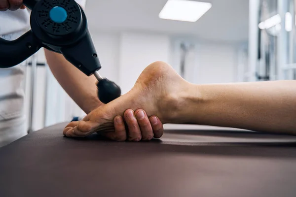 Detailní záběr masérky tření nohou ženy s masážním perkusním zařízením na rehabilitační klinice terapeutické místnosti — Stock fotografie