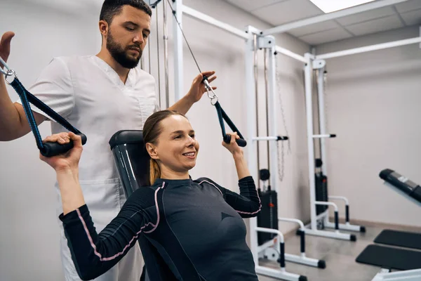 Kinesiologist assists young woman to do exercises to treat hand muscles and spine. Female patient — Stok fotoğraf