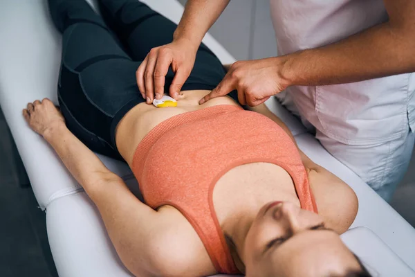 Therapeut plaatst elektrostimulator op de maag van de vrouw. Specialist in massagesalon zet elektroden — Stockfoto