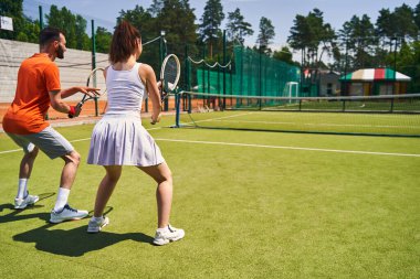 Eğitmen ve müşterisi düzgün bir tenis duruşu yapıyor.