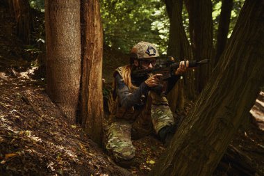 Asker oturuyor ve ateş etmek için silah tutuyor.