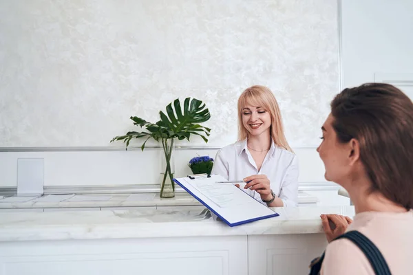 Beautiful receptionist checking registration list for procedure — Stockfoto