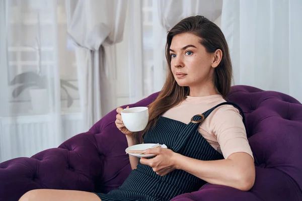 Söt ung kvinna njuter av sitt kaffe i salongen — Stockfoto