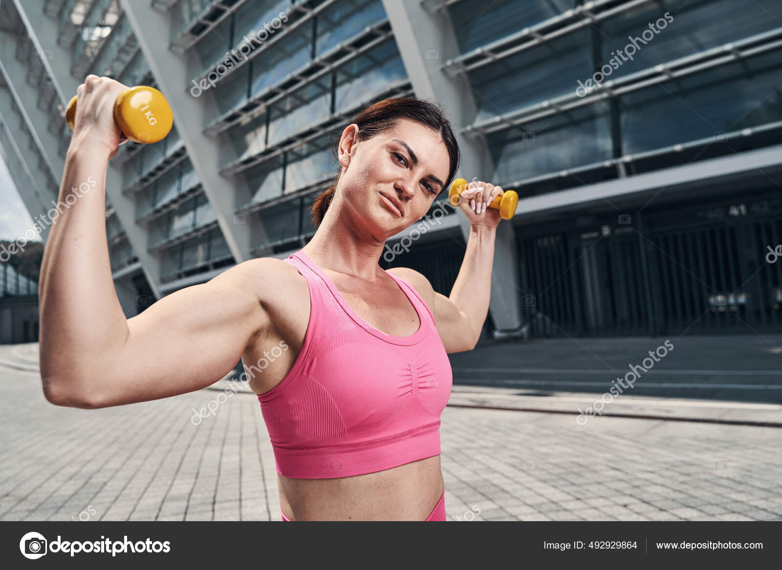 Female raising dumbbells in both hands in city Stock Photo by
