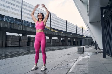 Neşeli kadın dışarıda çalışırken kollarını kaldırıyor.