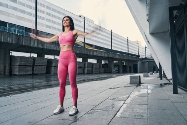 Beyaz tenli sporcu sokakta kollarını yana doğru sallıyor.