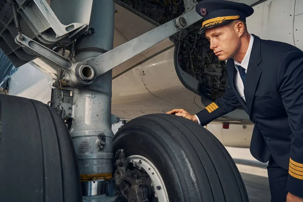 Aviador serio enfocado apoyado sobre las ruedas del avión — Foto de Stock