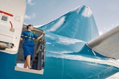 Gülümseyen uçuş görevlisi park halindeki bir uçaktan dışarı bakıyor.