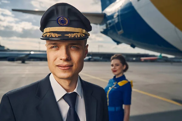 Piloto de la aerolínea y una azafata de cabello oscuro de pie en el aeródromo — Foto de Stock