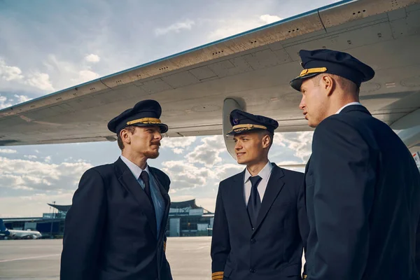 Tres pilotos caucásicos de pie junto a un ala de avión — Foto de Stock