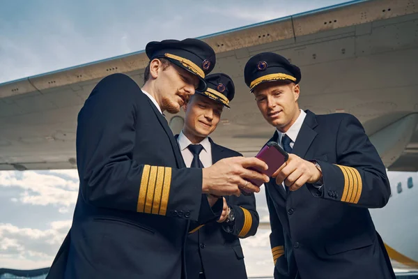 Piloto masculino demostrando el contenido de su celular a sus amigos — Foto de Stock