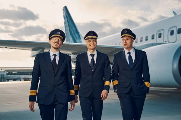 Tres pilotos guapos con estilo caminando por el aeródromo — Foto de Stock