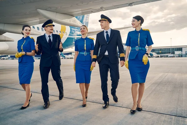 Beautiful stewardesses and handsome aviators walking along the airdrome — Stock Photo, Image