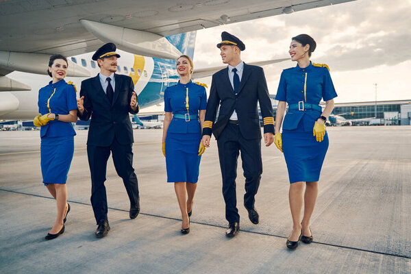 Beautiful stewardesses and handsome aviators walking along the airdrome