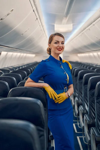 Piacevole hostess appoggiata al sedile della compagnia aerea in cabina — Foto Stock