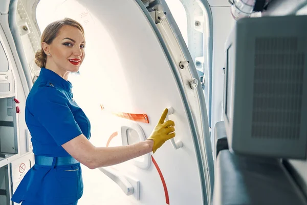 Esbelta azafata sonriente abriendo la puerta del avión —  Fotos de Stock