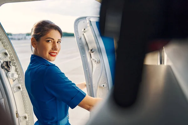 Adorável hospedeira de cabelos escuros abrindo a porta do avião — Fotografia de Stock