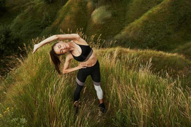 Uzun çimenlerde egzersiz yapan çekici sporcu bayan.