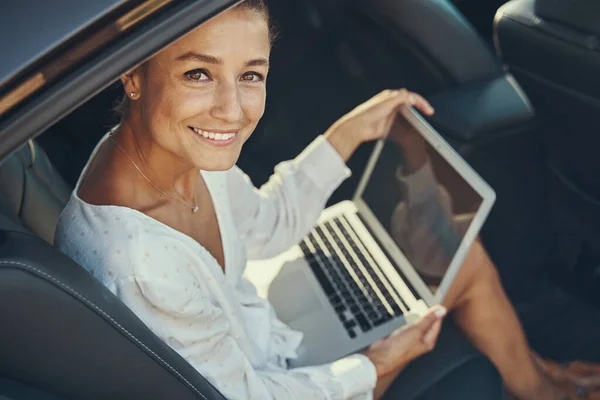 Mulher sentada com laptop perto da porta do carro aberta — Fotografia de Stock