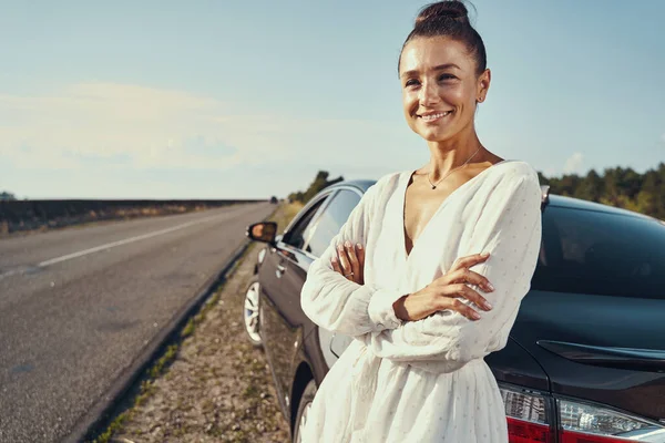 Mulher esperando ao lado de seu carro com sorriso otimista — Fotografia de Stock