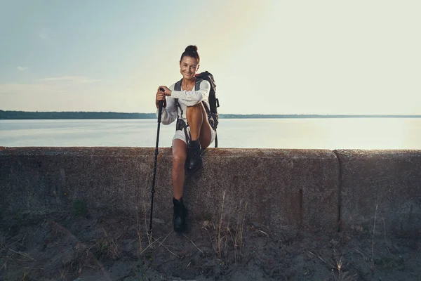 Femme excitée assise sur une barrière de pierre près du lac — Photo