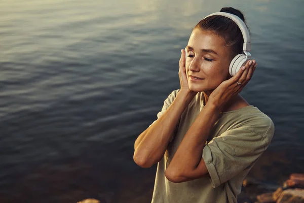 Mujer perdiéndose en la música a orillas del lago — Foto de Stock