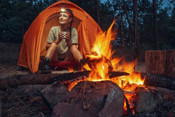 Person trinkt Tee vor Lagerfeuer im Zelt — Stockfoto